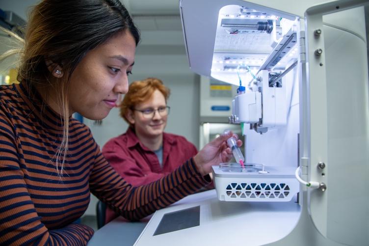 A male and female student work together in front of a piece of scientific equipment